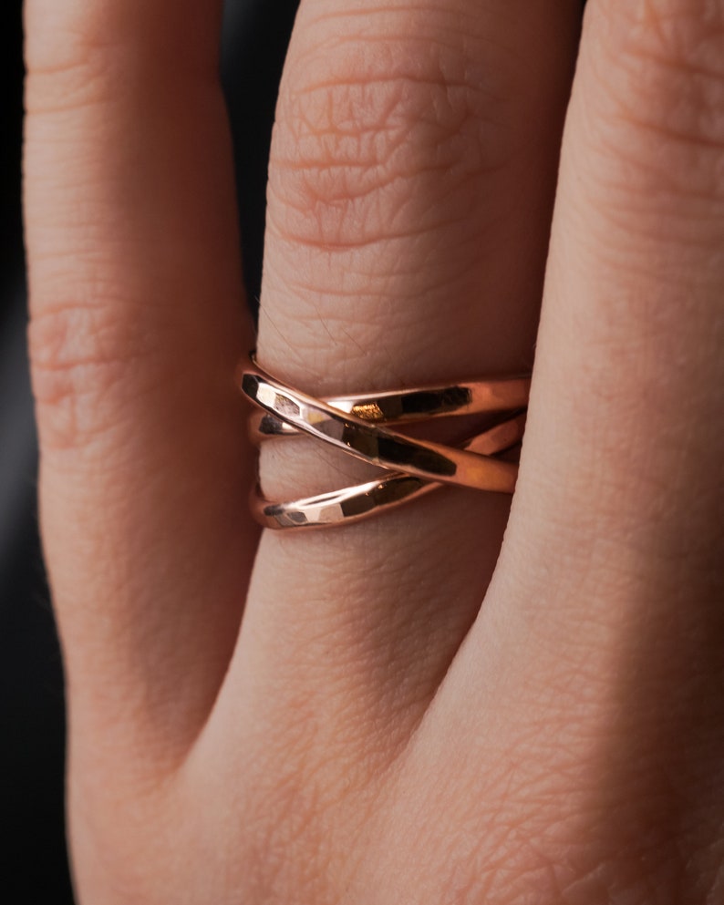Pu&ograve; includere: Un anello in oro rosa con un design a croce. L'anello &egrave; composto da tre bande intrecciate.