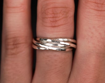 May include: A stack of four silver rings with a hammered texture. The rings are worn on a finger, with a yellow painted fingernail visible in the background. The rings have a textured, hammered finish.