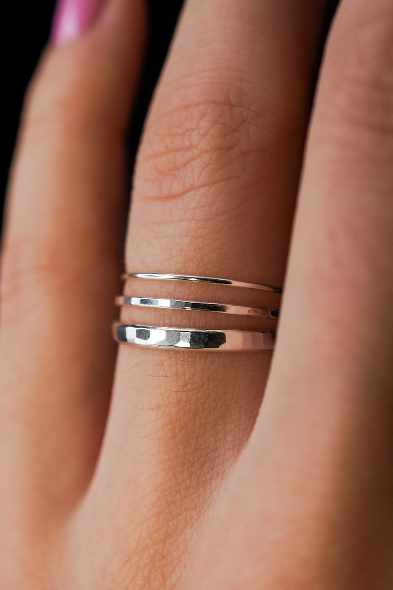 May include: Three silver rings stacked on a finger. The bottom ring is hammered and the top two are smooth.