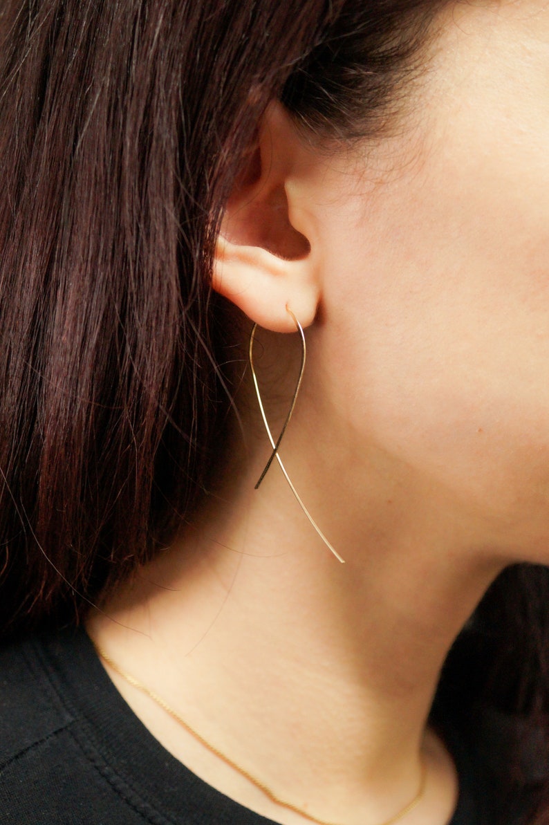 Large Ribbon Hoops that thread through an earlobe piercing and dangle. Modelled in 14K Gold Fill. Thin wire earrings, easy and functional to wear. Shaped like cancer awareness ribbon.