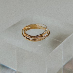 Pode incluir: Tr&ecirc;s an&eacute;is de ouro empilhados um em cima do outro. Os an&eacute;is s&atilde;o lisos e t&ecirc;m uma textura ligeiramente martelada.