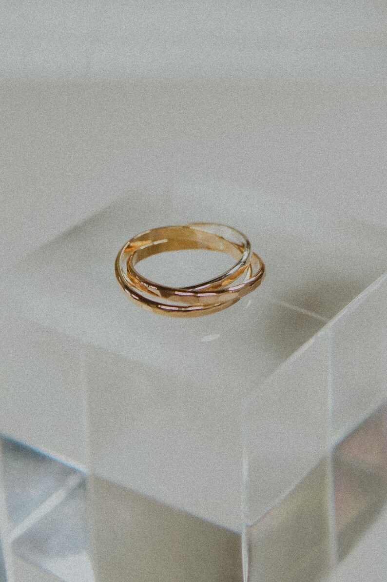 Pode incluir: Tr&ecirc;s an&eacute;is de ouro empilhados um em cima do outro. Os an&eacute;is s&atilde;o lisos e t&ecirc;m uma textura ligeiramente martelada.