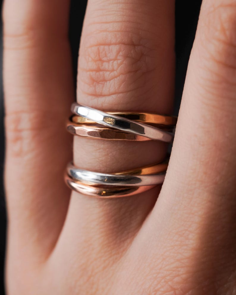 Pode incluir: Um conjunto de tr&ecirc;s an&eacute;is entrela&ccedil;ados, um de prata, um de ouro rosa e um de cobre martelado. Os an&eacute;is s&atilde;o usados em um dedo.