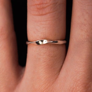 May include: A thin, gold, wavy wedding band worn on a finger.