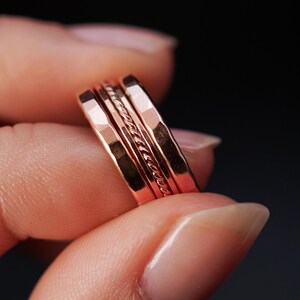 Op de afbeelding: Een set van vier stapelringen van roségoud. De ringen zijn allemaal van verschillende breedtes en hebben een gehamerde textuur. De bovenste ring heeft een gedraaid draadontwerp.