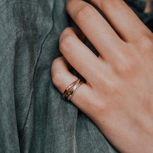 Pode incluir: Um close-up de uma m&atilde;o usando um anel entrela&ccedil;ado de ouro, prata e ouro rosa.