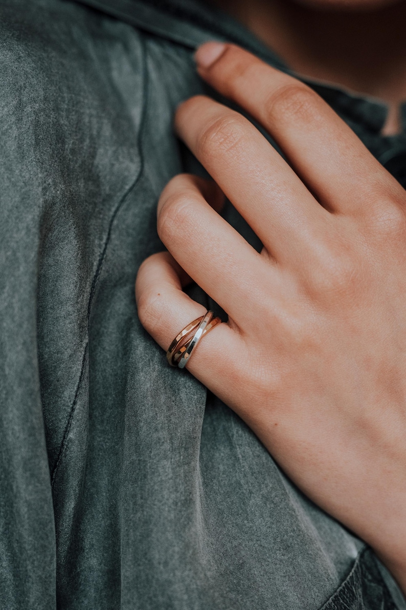 Pode incluir: Um close-up de uma m&atilde;o usando um anel entrela&ccedil;ado de ouro, prata e ouro rosa.