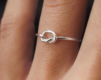 May include: A silver knot ring on a finger.