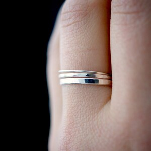May include: Three silver stacking rings on a finger. The rings are hammered and have a slightly textured finish.