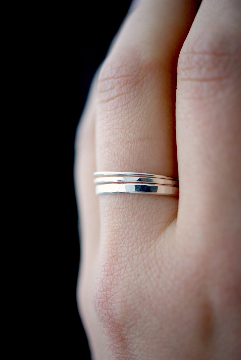 May include: Three silver stacking rings on a finger. The rings are hammered and have a slightly textured finish.