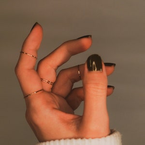 Dainty stacking rings worn on the index and middle finger. great on their own, as midi rings and stacked together. Modelled with a white sweater and dark nail polish.