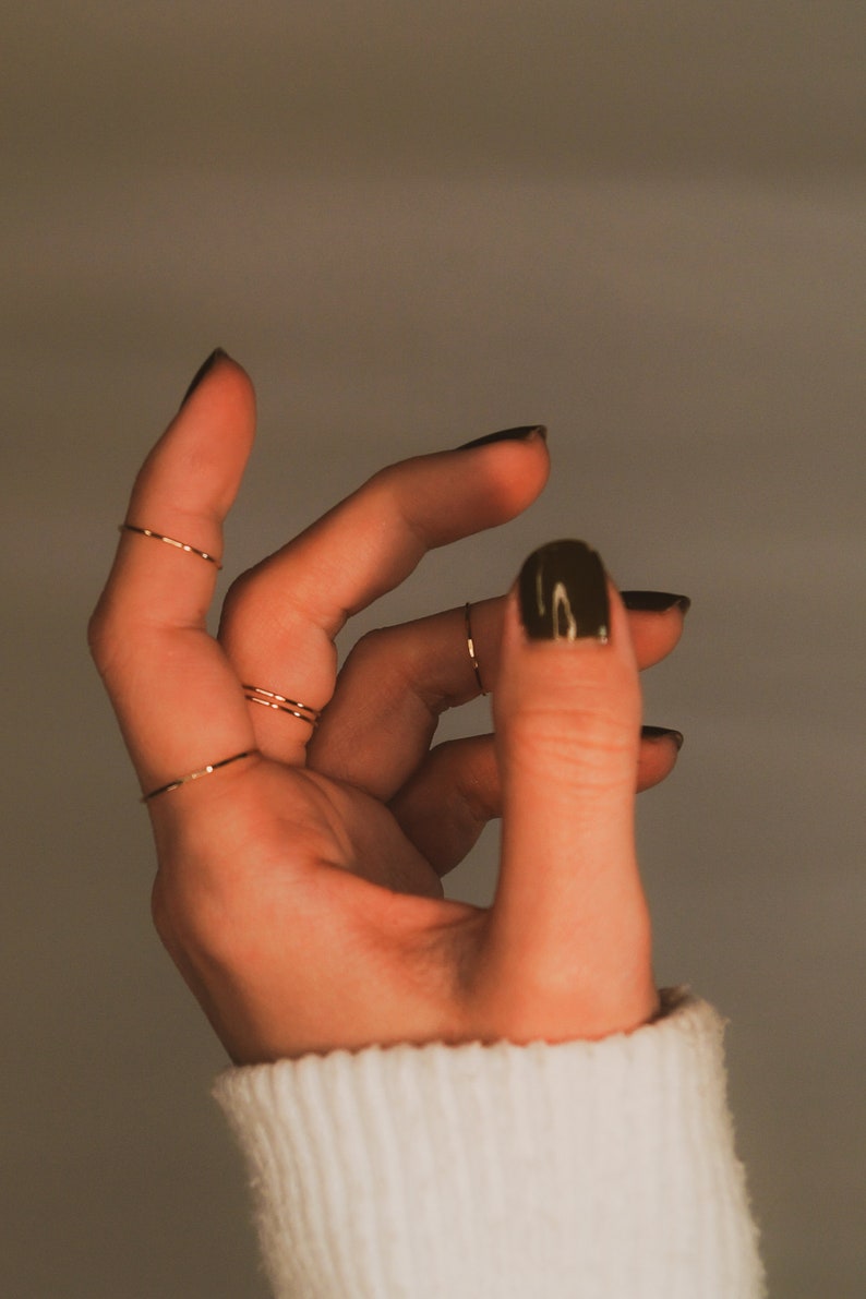 Dainty stacking rings worn on the index and middle finger. great on their own, as midi rings and stacked together. Modelled with a white sweater and dark nail polish.