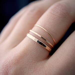 May include: Three gold rings stacked on a finger. The bottom ring is hammered, the middle ring is smooth, and the top ring is smooth.