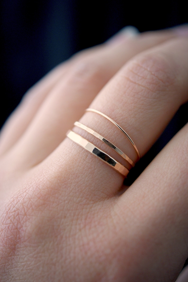 May include: Three gold rings stacked on a finger. The bottom ring is hammered, the middle ring is smooth, and the top ring is smooth.