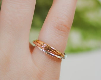 May include: A three-band ring with a silver, rose gold, and gold finish. The ring is worn on a finger.