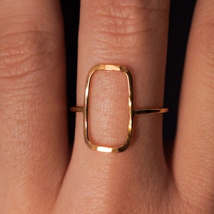 May include: A gold ring with a hammered, rectangular shape. The ring is open and has a smooth, polished finish.