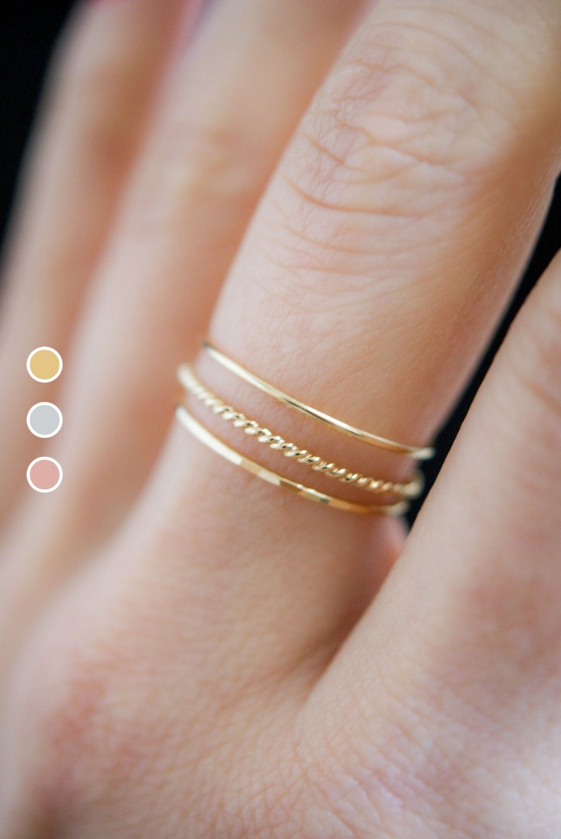 Close up view of three gold stacking rings modeled on a middle finger. One twist ring with one smooth and one hammered ring.