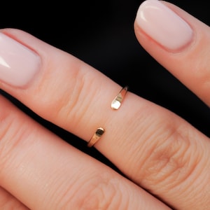 Puede incluir: Un anillo abierto dorado usado en un dedo con esmalte de uñas rosa claro.