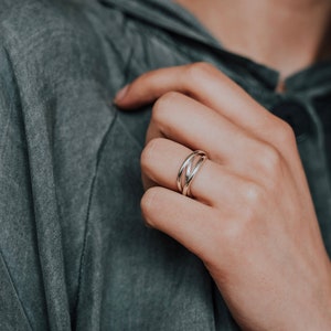 Pu&ograve; includere: Un anello d'argento con tre bande intrecciate. L'anello &egrave; su un dito.