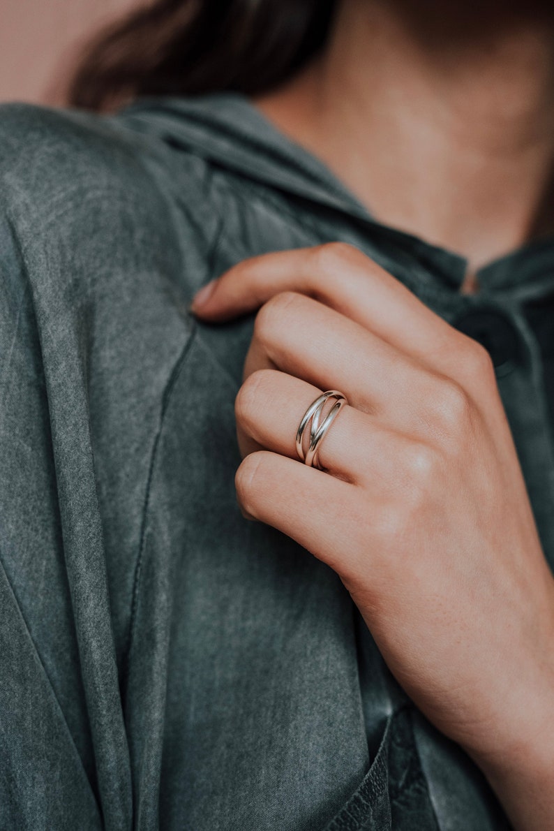 Pu&ograve; includere: Un anello d'argento con tre bande intrecciate. L'anello &egrave; su un dito.