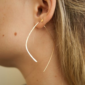 Puede incluir: Un par de pendientes de aro de oro con un diseño curvo único. Los pendientes están hechos de metal fino y tienen un aspecto simple y elegante.