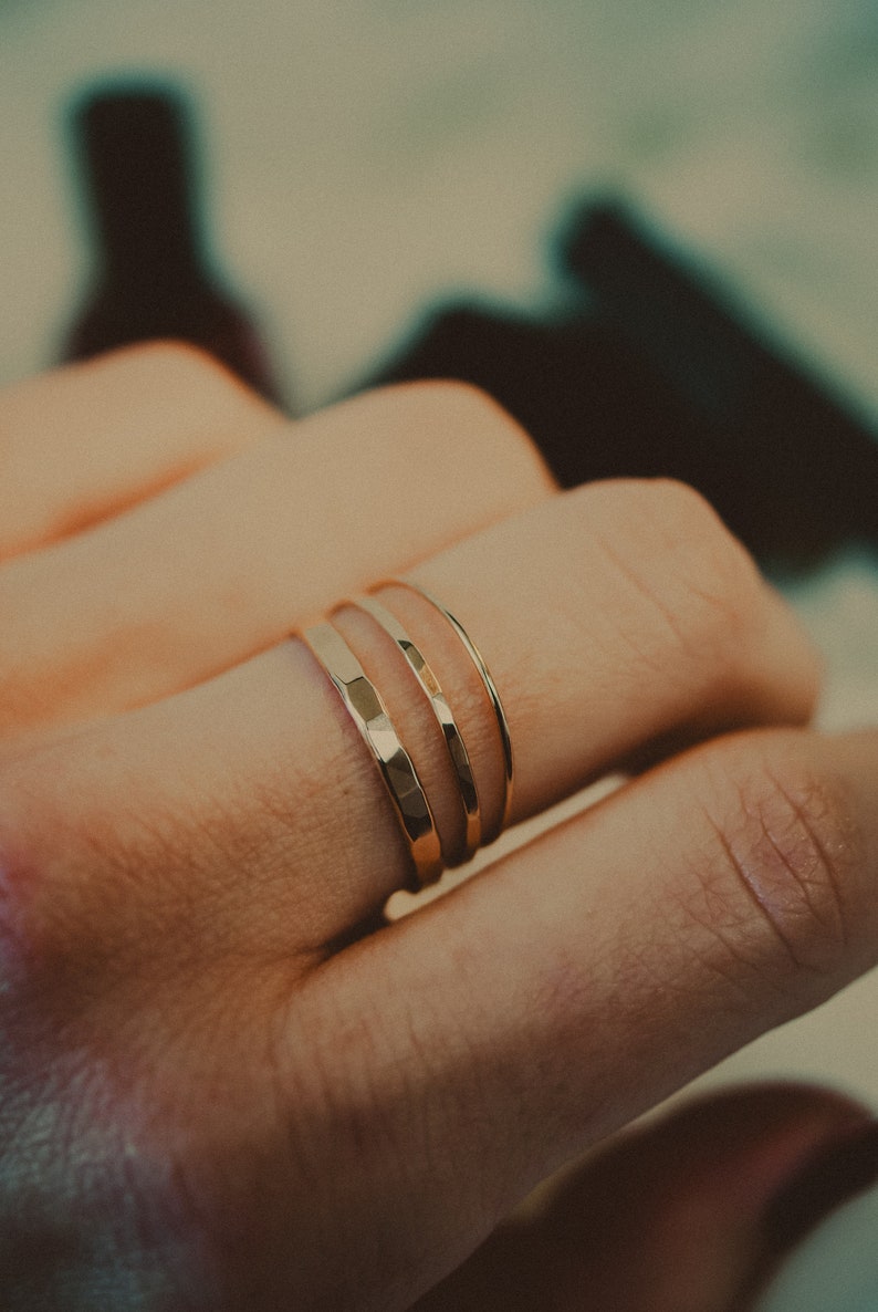 May include: Three gold rings stacked on a finger. The rings are all different widths and have a hammered texture.