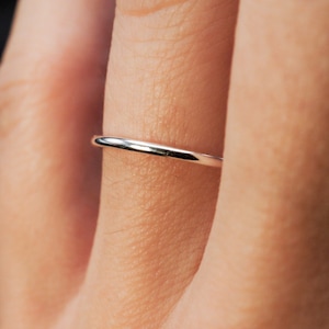 May include: A simple, thin, silver band ring worn on a finger.