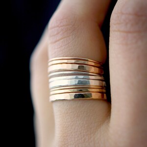 May include: A stack of hammered gold and silver rings on a finger.