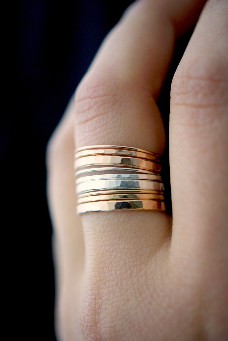 May include: A stack of hammered gold and silver rings on a finger.