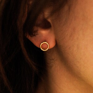 May include: A close-up of a person's ear with a small, gold, circular earring.