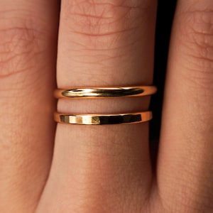 May include: Two gold rings stacked on a finger. The top ring is smooth and the bottom ring has a hammered texture.
