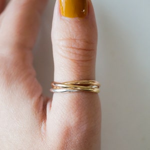 Pode incluir: Um anel de tr&ecirc;s bandas em ouro, prata e ouro rosa em um dedo com esmalte de unha amarelo.