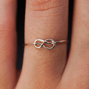 May include: A delicate silver infinity knot ring worn on a finger.