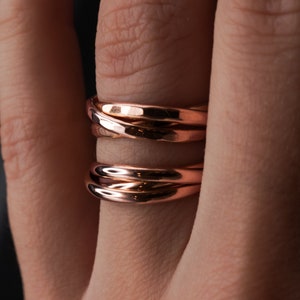 Pu&ograve; includere: Un anello in oro rosa con finitura martellata. L'anello &egrave; composto da tre bande intrecciate.