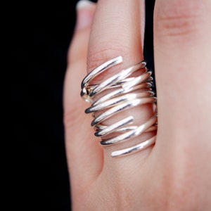 Könnte beinhalten: Ein silberner Ring mit einem einzigartigen Design aus mehreren ineinander verschlungenen Bändern, die einen Spiraleffekt erzeugen.