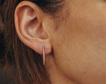May include: A close-up of a person's ear with a thin gold bar earring.