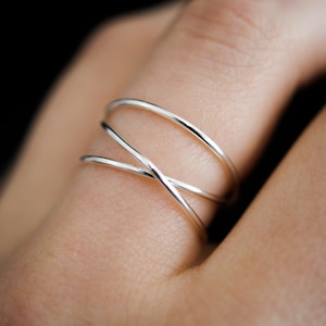 Puede incluir: Un anillo de plata con múltiples bandas entrelazadas. El anillo se lleva en un dedo.