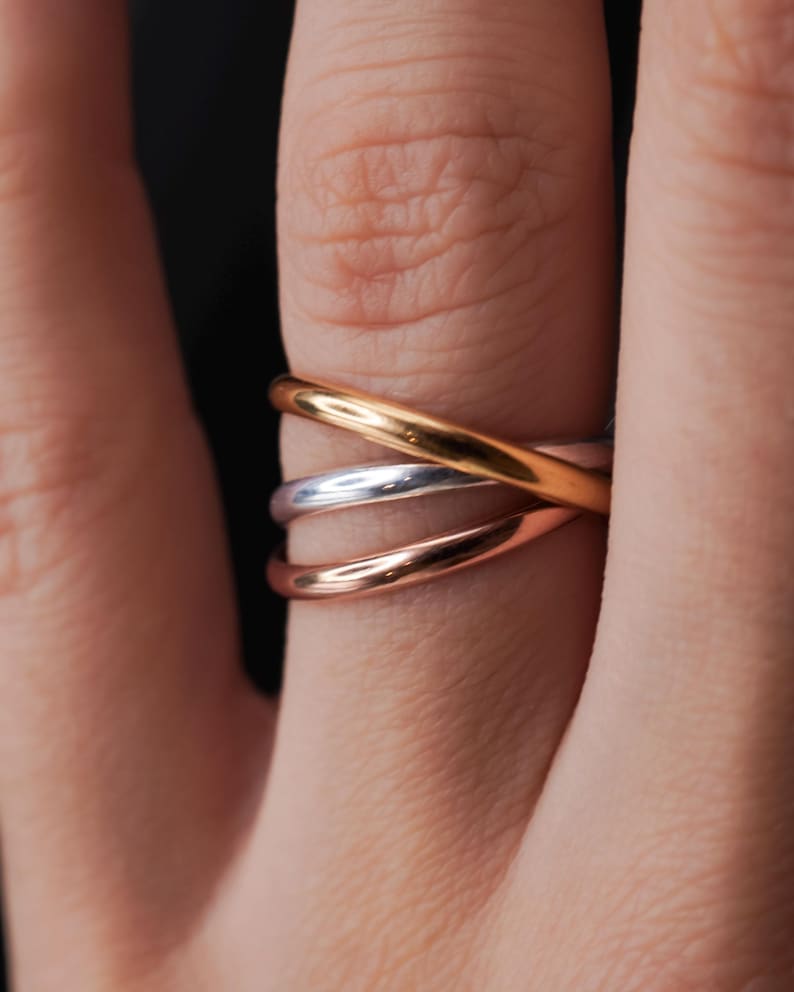 Pode incluir: Um anel entrela&ccedil;ado de ouro, prata e ouro rosa usado em um dedo.