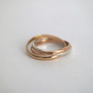 Pode incluir: Um conjunto de tr&ecirc;s an&eacute;is entrela&ccedil;ados, um de ouro, um de prata e um de ouro rosa. Os an&eacute;is s&atilde;o lisos e polidos.