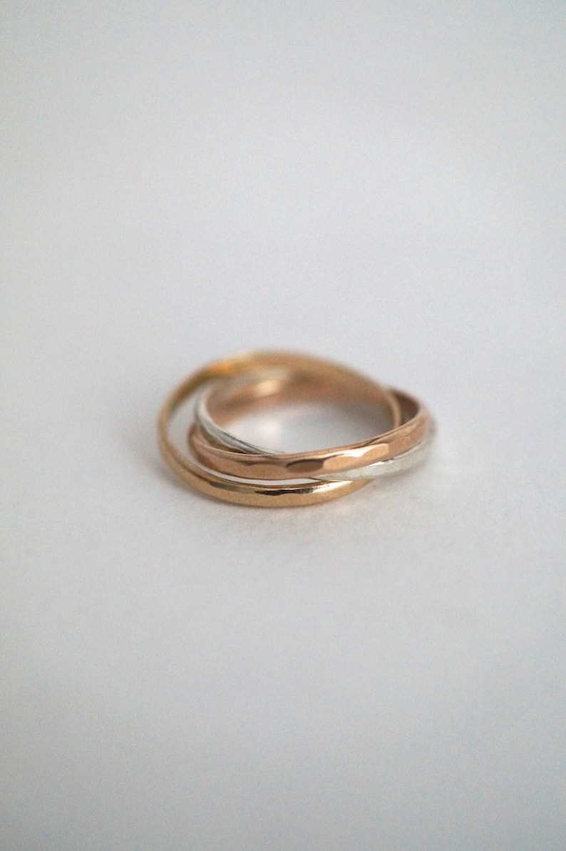 Pode incluir: Um conjunto de tr&ecirc;s an&eacute;is entrela&ccedil;ados, um de ouro, um de prata e um de ouro rosa. Os an&eacute;is s&atilde;o lisos e polidos.