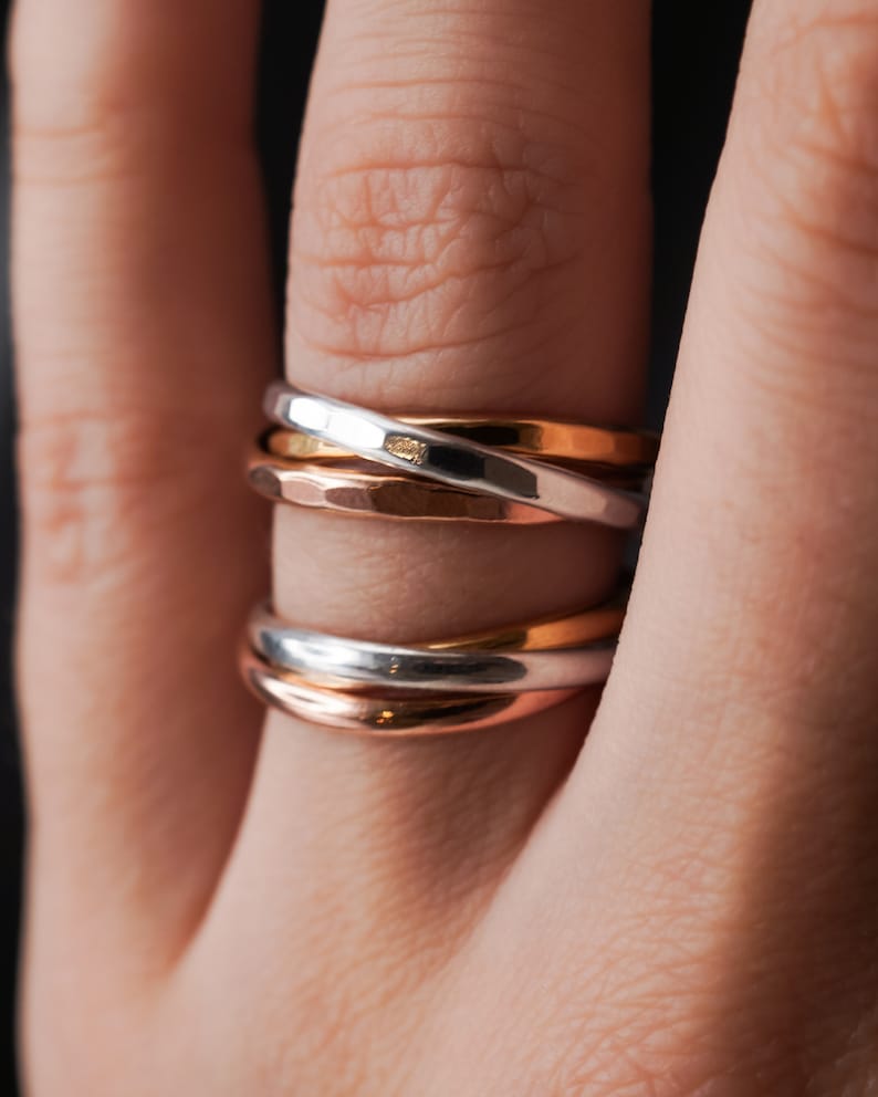 Pu&ograve; includere: Un set di tre anelli intrecciati, uno in argento, uno in oro rosa e uno in oro. Gli anelli sono indossati su un dito.