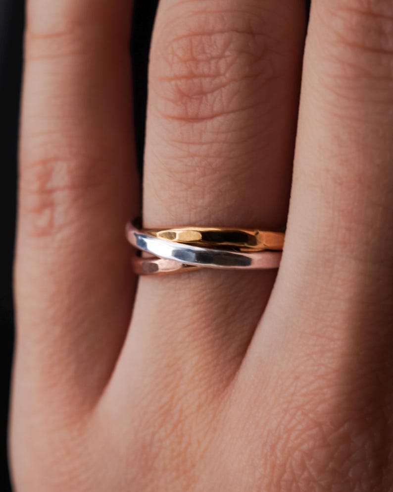 Pode incluir: Um anel de tr&ecirc;s bandas com acabamento prata, ouro rosa e ouro. O anel &eacute; usado em um dedo.