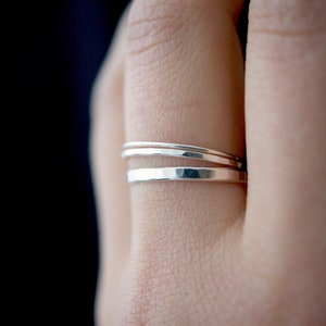 May include: Three silver stacking rings on a finger. The rings are thin and have a hammered texture.