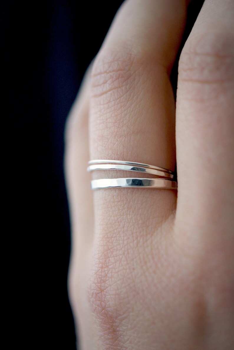 May include: Three silver stacking rings on a finger. The rings are thin and have a hammered texture.