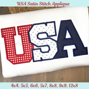 Op de afbeelding: Witte stof met het woord "USA" in rode, witte en blauwe satijnsteek applicatie. De letter "U" is rood met een ruitpatroon, "S" is wit met blauwe stippen en "A" is marineblauw met witte stippen. De tekst bovenaan luidt "USA Satin Stitch Applique".