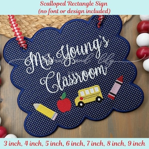 May include: A navy blue, scalloped-edge sign with white polka dots and the text "Mrs. Young's Classroom." The sign features embroidered images of a yellow school bus, a red apple, a pink crayon, and a yellow pencil. Sizes available: 3 to 9 inches.