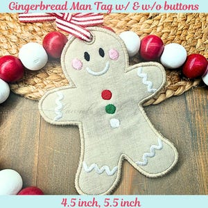 May include: A beige gingerbread man tag with embroidered details, including a smiling face, pink cheeks, and colorful button accents. The tag is approximately 4.5 inches and 5.5 inches. It has a red and white striped ribbon for hanging. The text "Gingerbread Man Tag w/ & w/o buttons" is at the top.