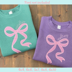 May include: Two crew neck sweatshirts, one teal and one purple, with embroidered pink bows and names. The teal sweatshirt has the name "Caroline" embroidered above the bow. The purple sweatshirt has the name "Aubrey" embroidered above the bow. The text "Font not included" is at the top.