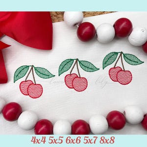 May include: White fabric with three embroidered cherry designs. Each cherry cluster has two red cherries, green leaves, and brown stems. A red bow and red and white beads are in the background. The text at the bottom reads "4x4 5x5 6x6 5x7 8x8".