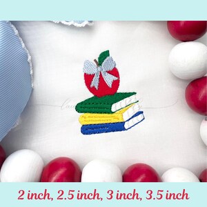 May include: An embroidered design of a red apple with a blue bow on top of three books. The books are green, yellow, and blue. The text at the bottom reads "2 inch, 2.5 inch, 3 inch, 3.5 inch".
